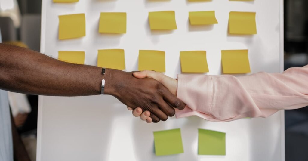 pexels-photo-7710082-7710082 Colleagues shaking hands in front of a marketing board during a business meeting.